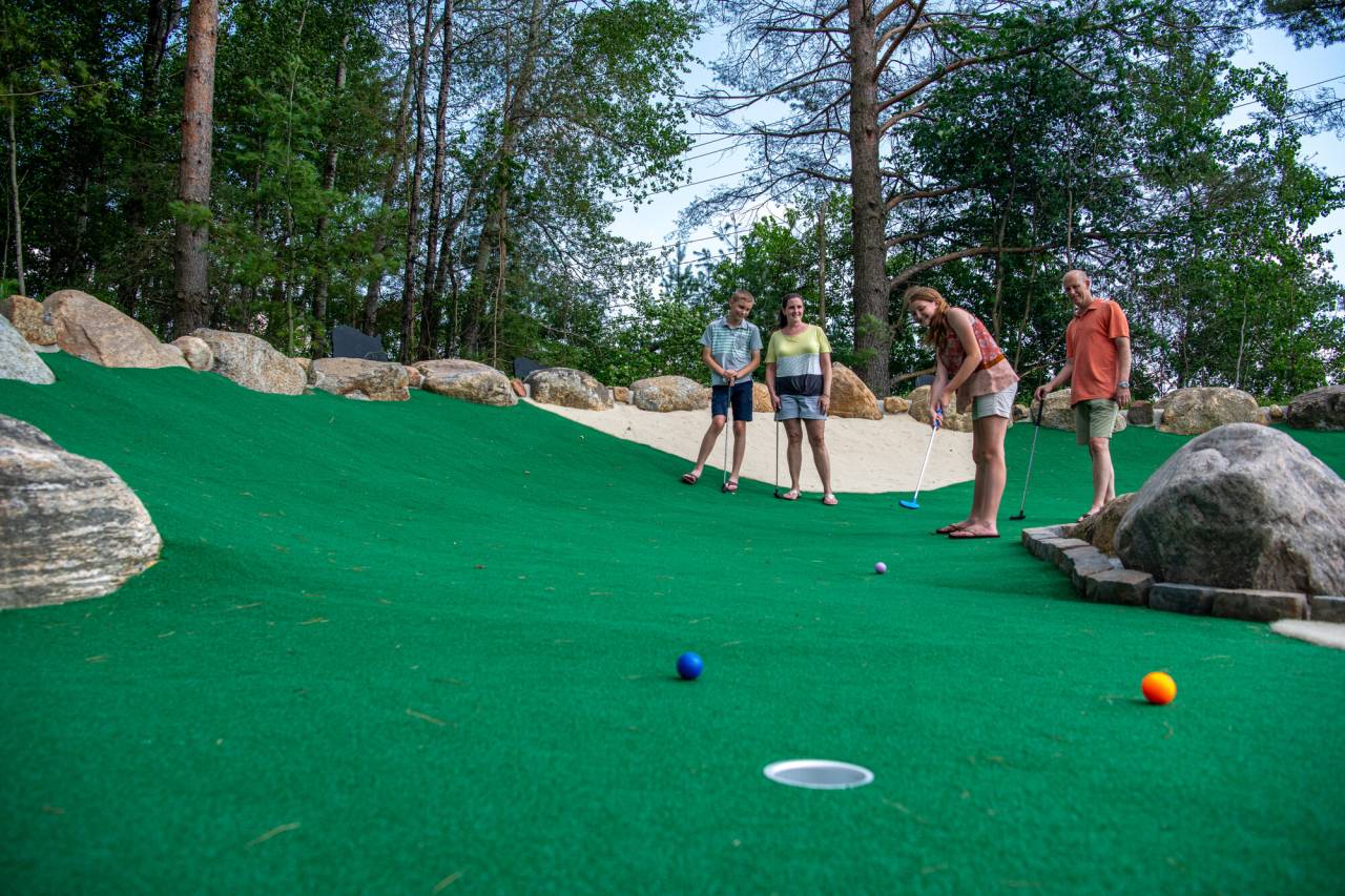 A family plays mini golf on a sloped course. 